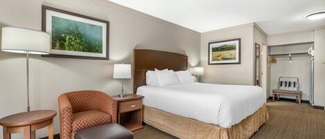 A hotel room with a large bed, a chair, a small table, and a bench.
