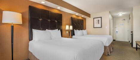 Habitación de hotel con dos camas, un cabecero grande, una lámpara de pie y una puerta al fondo.