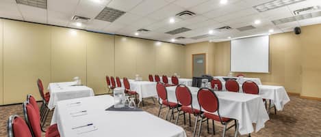 A conference room with multiple tables and chairs, equipped with nameplates, water bottles, and a projector screen.