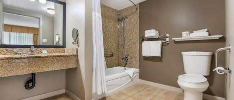 A bathroom with a granite countertop, a shower, a toilet, and a mirror.