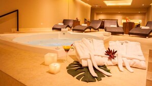 Zona de spa con una bañera de hidromasaje, sillas de descanso, toallas y velas.