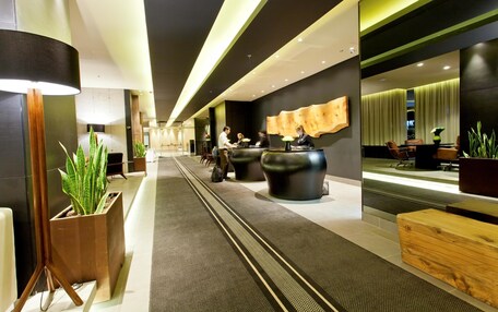 A modern hotel lobby with a reception desk, seating area, and potted plants.