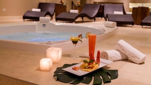 Zona de spa con hidromasaje, sillones reclinables, velas, una bandeja de fruta y un cóctel.