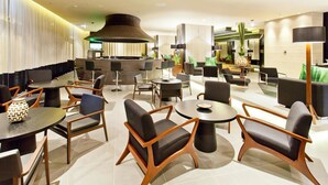Un moderno vestíbulo de hotel con mesas redondas, asientos cómodos, una zona de bar y un espejo grande.