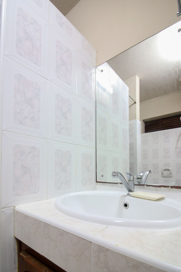 Un baño con lavamanos, espejo y paredes de azulejos.