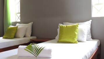 A hotel room with two beds, each with white linens and green pillows.