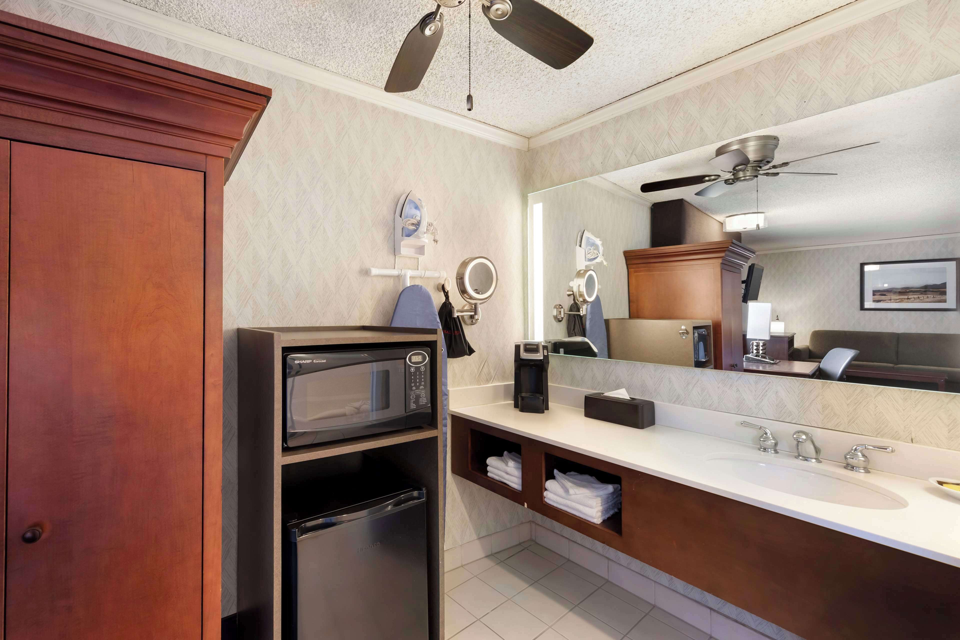 A modern bathroom with a wooden vanity, a built-in microwave, a coffee maker, and a large mirror.
