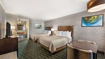 A hotel room with two beds, a desk, a chair, a TV, a lamp, and a painting on the wall.