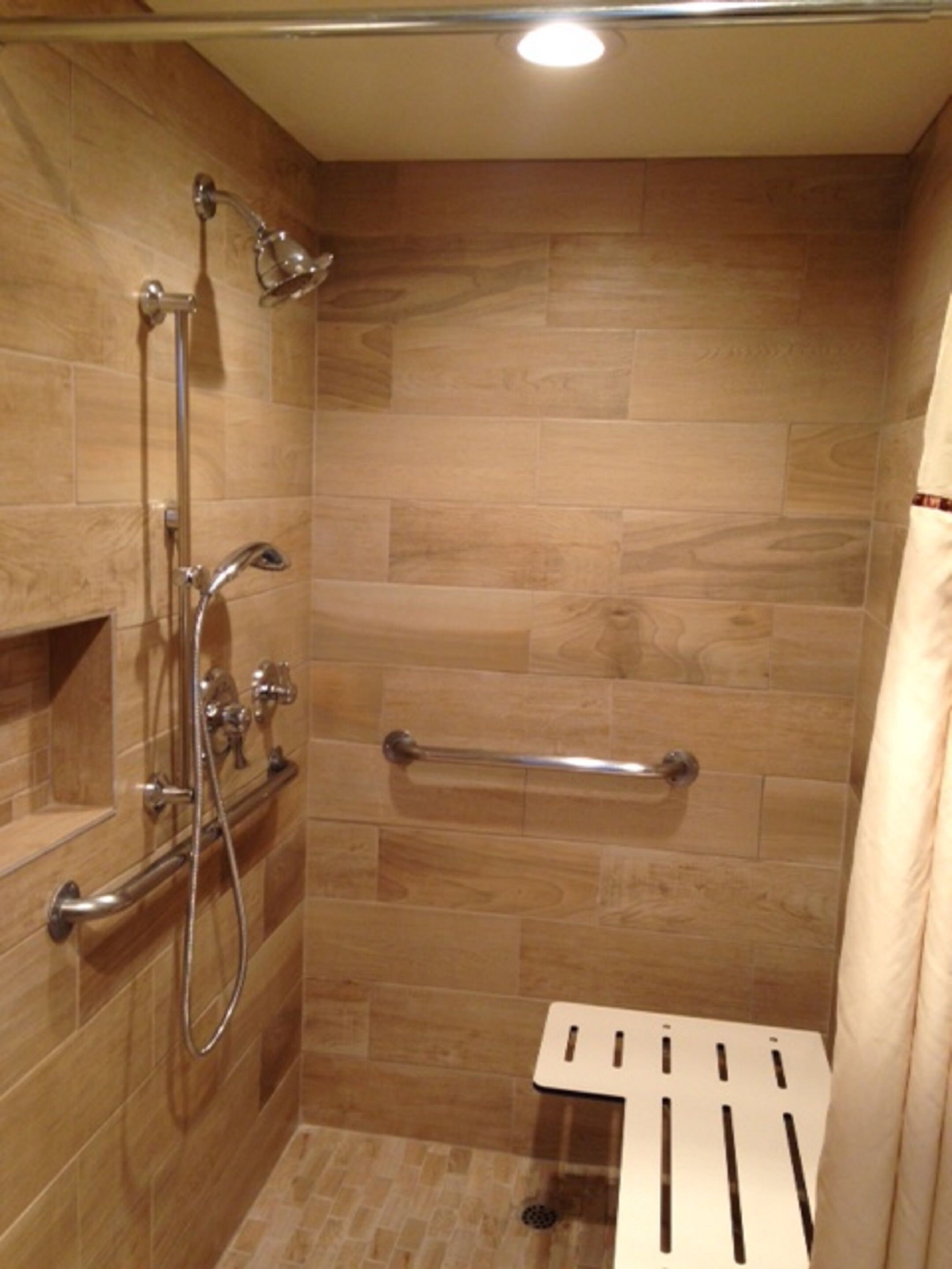 Eine Dusche mit Glastür, Handläufer und Duschkopf.