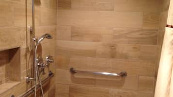 Ducha con puerta de vidrio, barra de apoyo y cabezal de ducha.