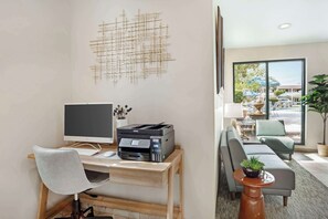 Un espacio de oficina moderno con escritorio, computadora, impresora y vista al área de asientos exteriores.