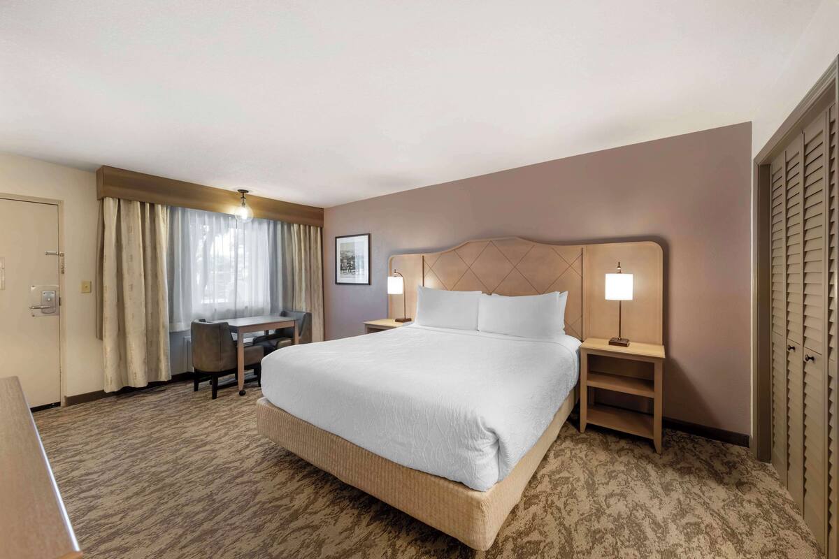 Quarto de hotel com uma cama grande, uma escrivaninha e uma cadeira. Há uma luminária em cada lado da cama.
