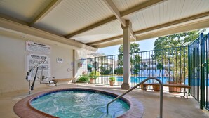 Zona con jacuzzi cubierto, piscina al fondo, carteles de advertencia y un banco.
