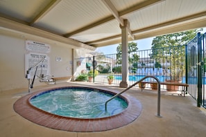 A covered hot tub area with a pool in the background, warning signs, and a bench. - Best Western Plus Black Oak (Paso Robles)