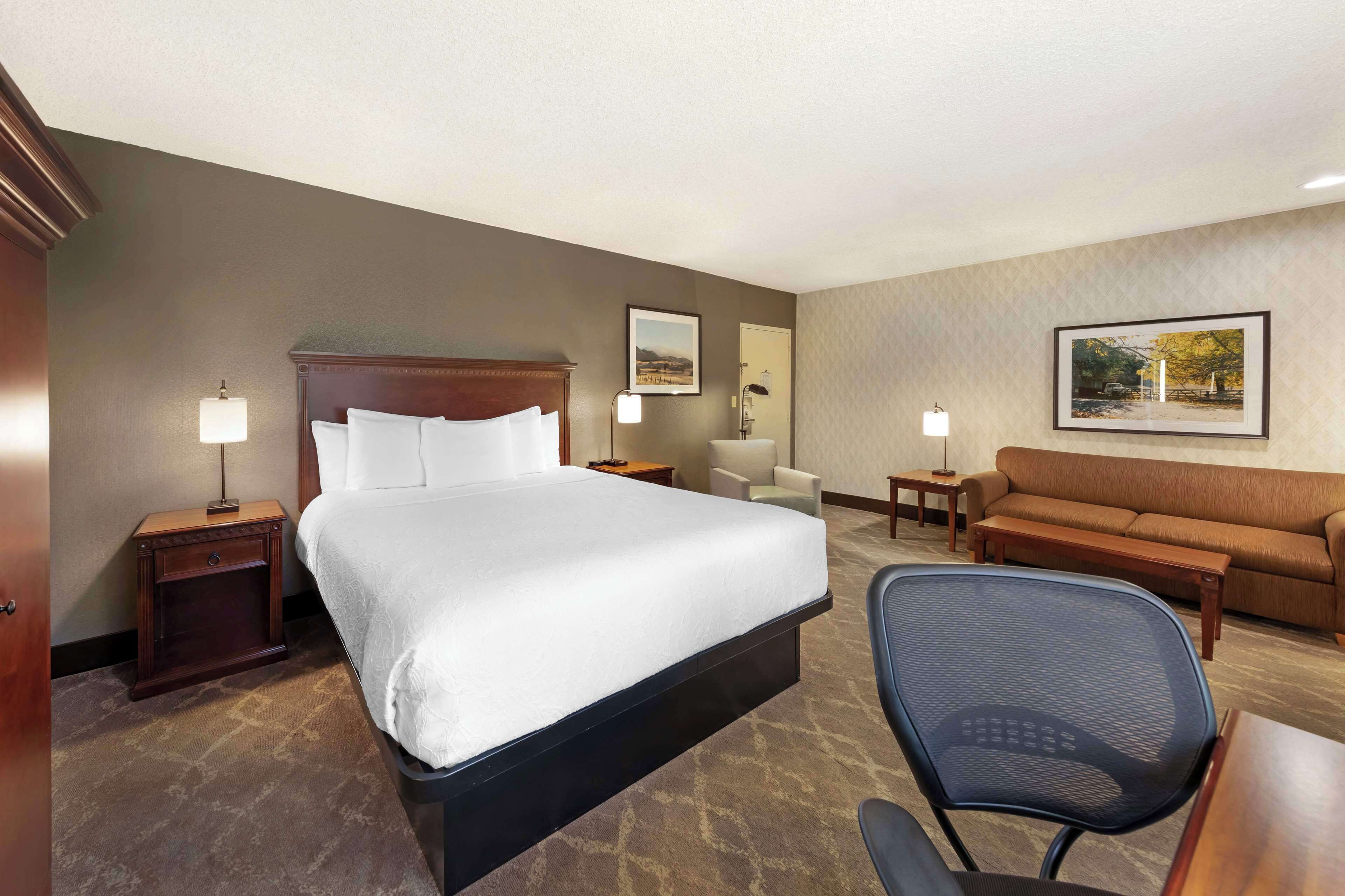 A hotel room with a large bed, a desk, a chair, a sofa, and two lamps.