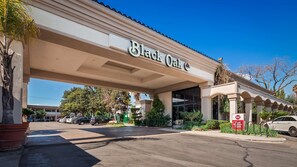 A hotel entrance with a covered walkway, a sign reading 'Black Oak,' and a parking area with cars.