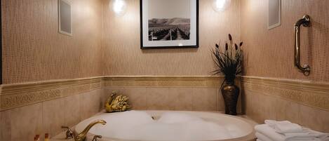 A bathroom with a large bathtub, a wall-mounted mirror, and a framed picture above the mirror.