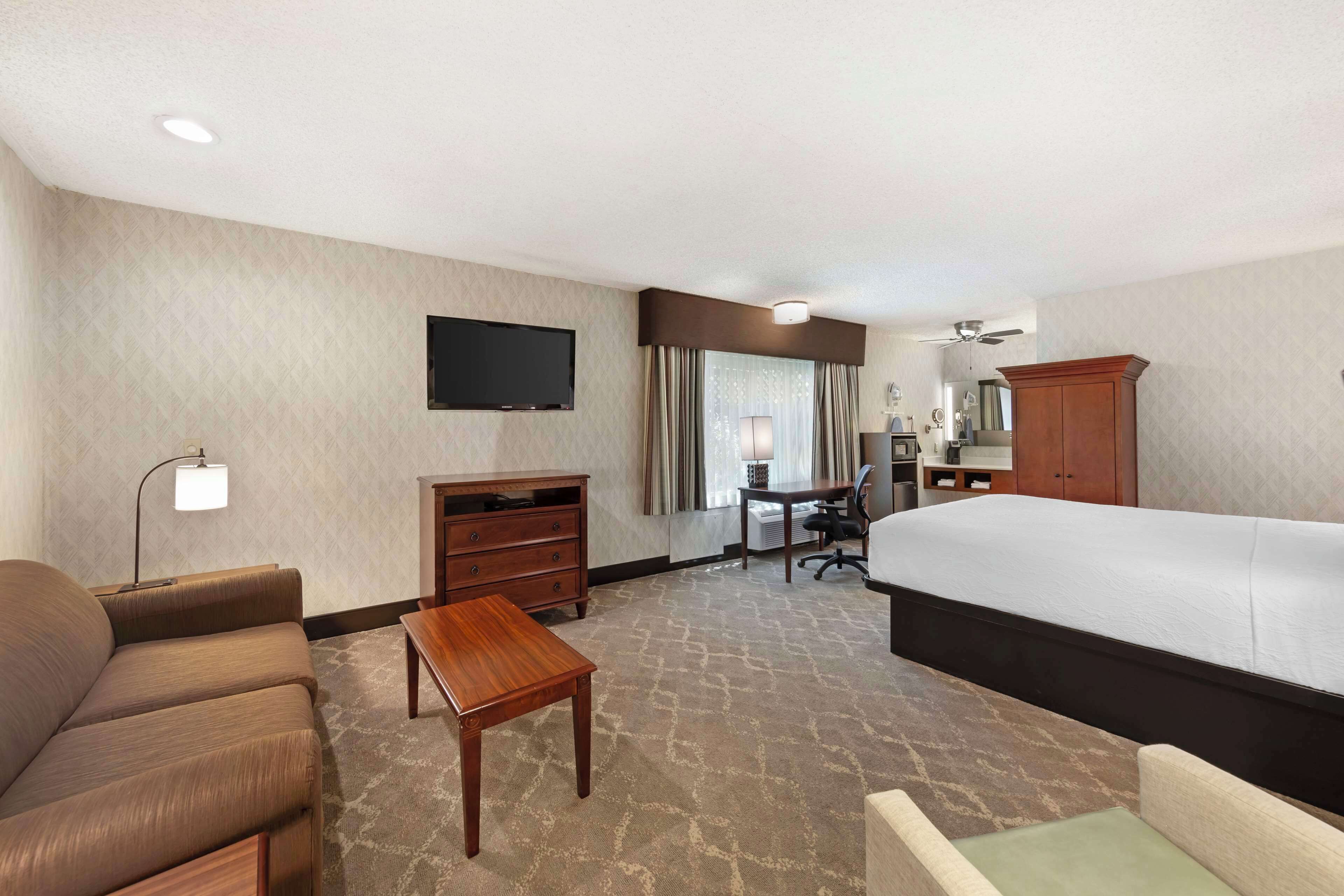 A hotel room with a bed, a desk, a chair, a sofa, a TV, and a wardrobe.