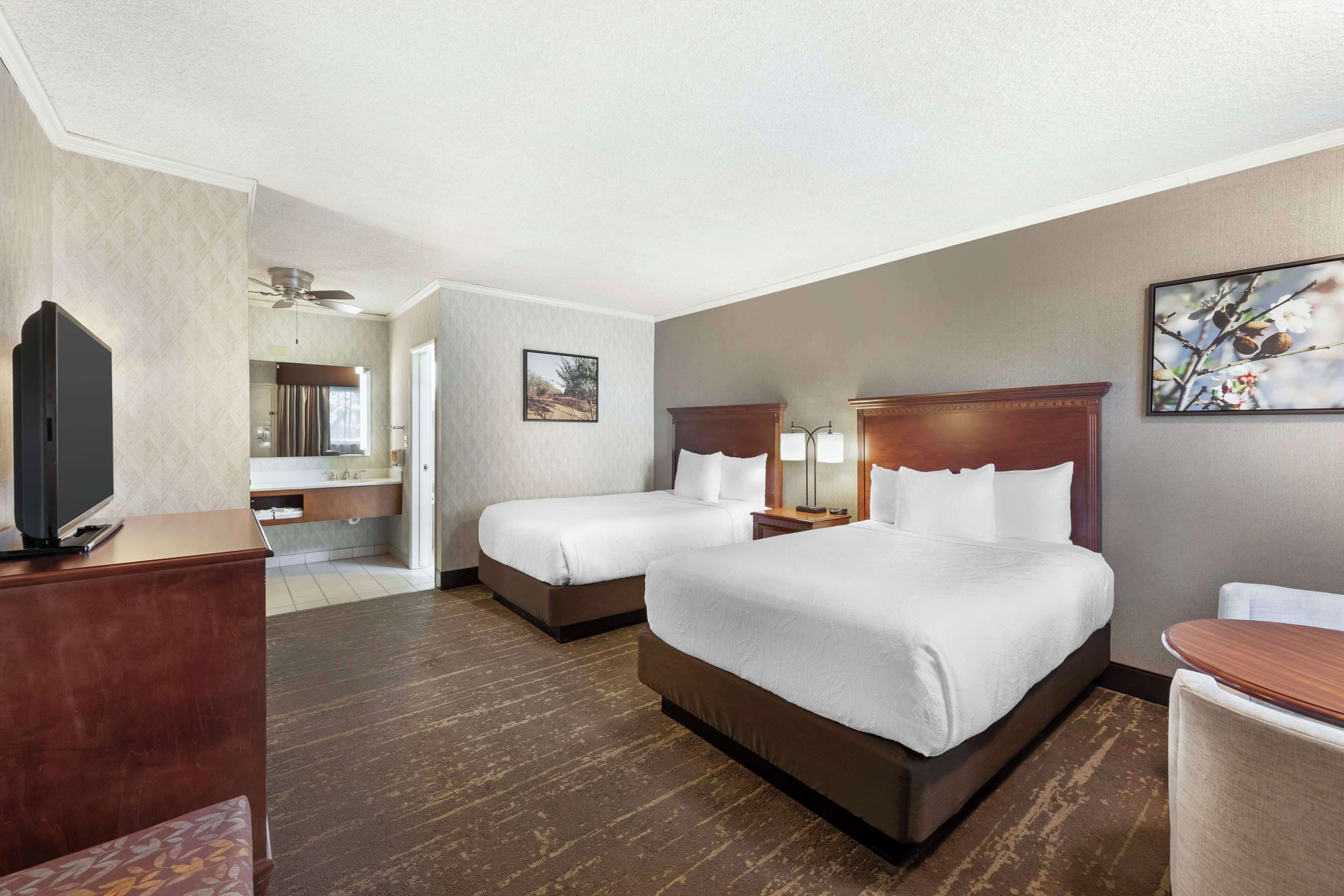 A hotel room with two beds, a TV, a desk, and a bathroom.