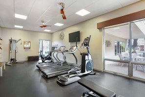 Een sportschool met loopbanden, elliptische trainers en een bank.