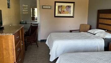 A hotel room with two beds, a wooden dresser, a desk, and a framed welcome sign.