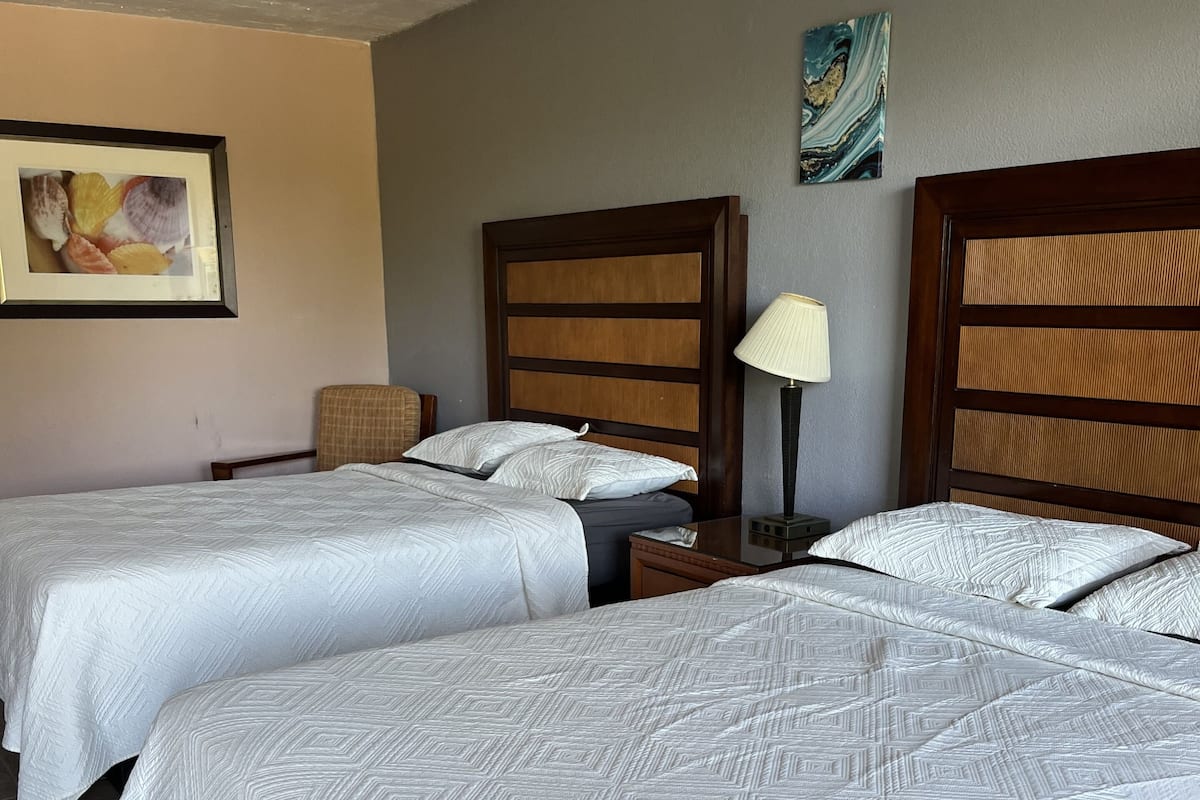 Una habitación de hotel con dos camas, una mesita de noche, una lámpara y un cuadro en la pared.