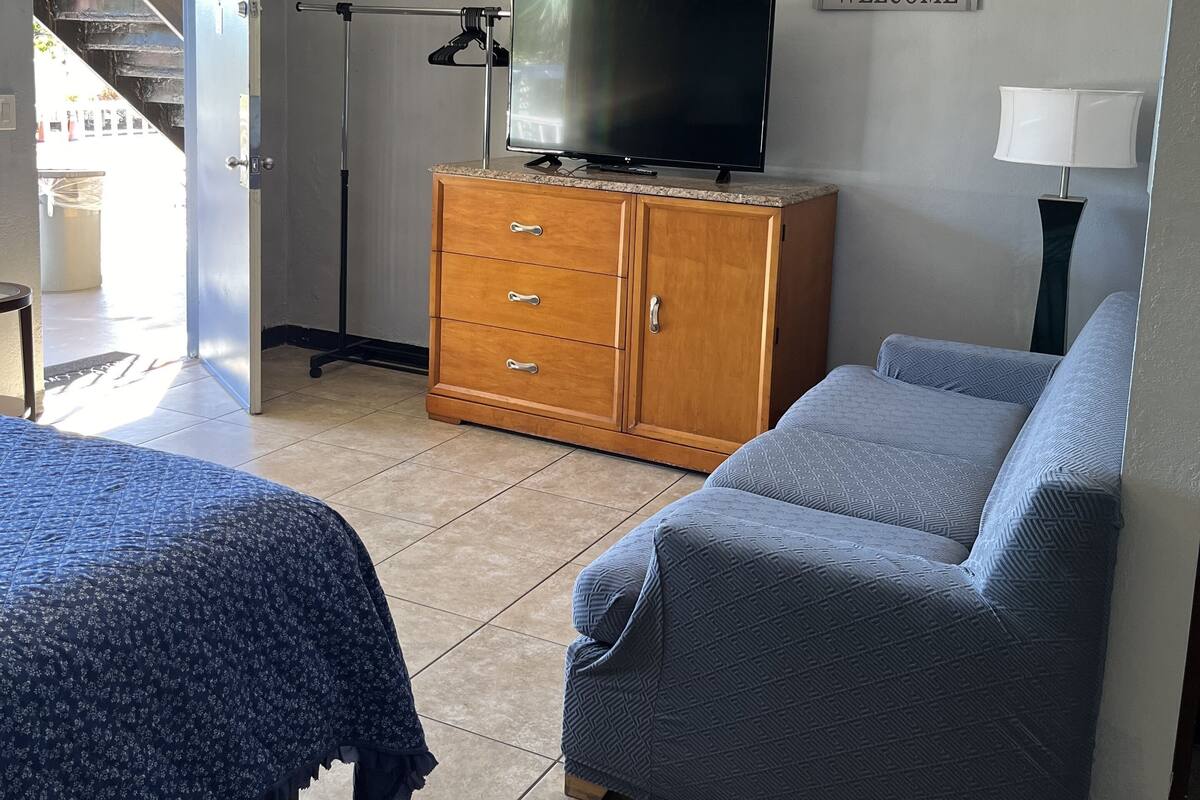 Una habitación de hotel con una cama, un sofá, un televisor sobre un mueble de madera, una lámpara y un cartel que dice 'WELCOME' en la pared.