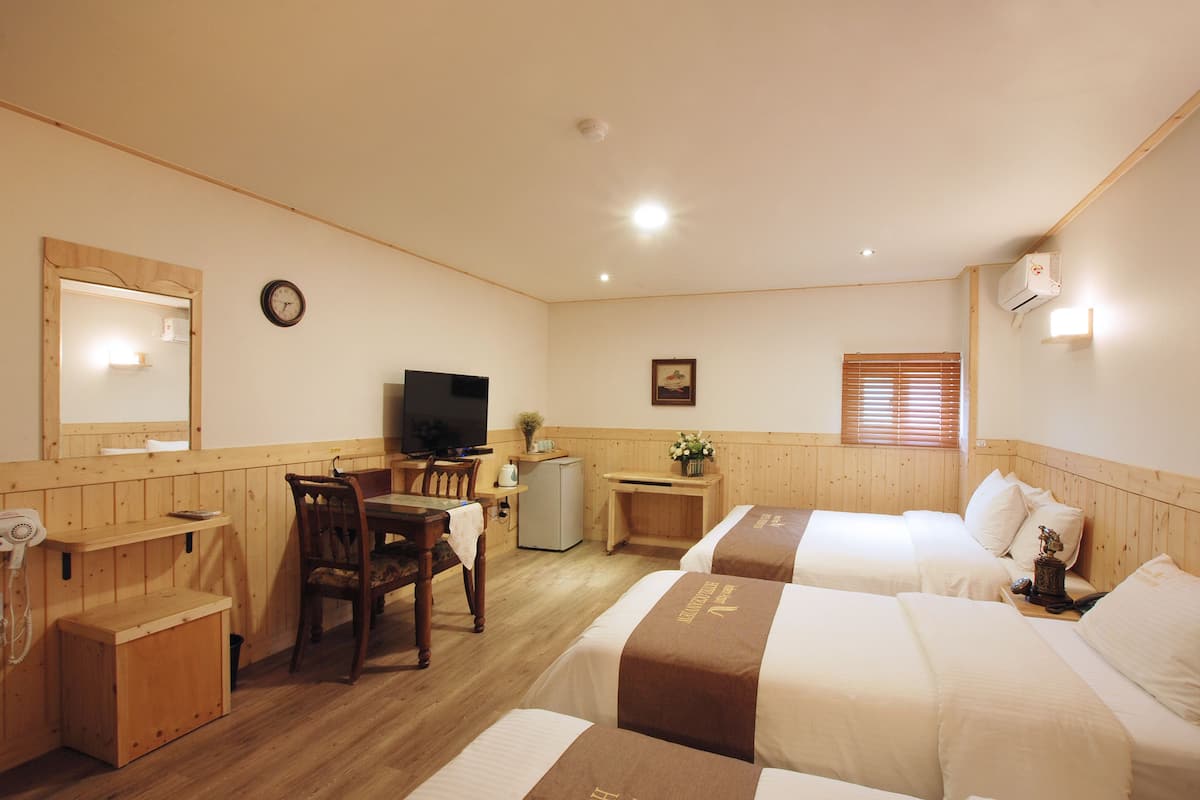 Habitació d'hotel amb dos llits, una taula, una cadira, un televisor, un mirall i una cuineta petita.