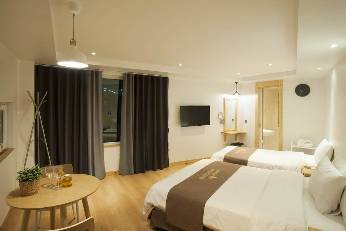 Habitació d'hotel amb dos llits, una televisió, una taula de fusta amb una planta i una finestra amb cortines.