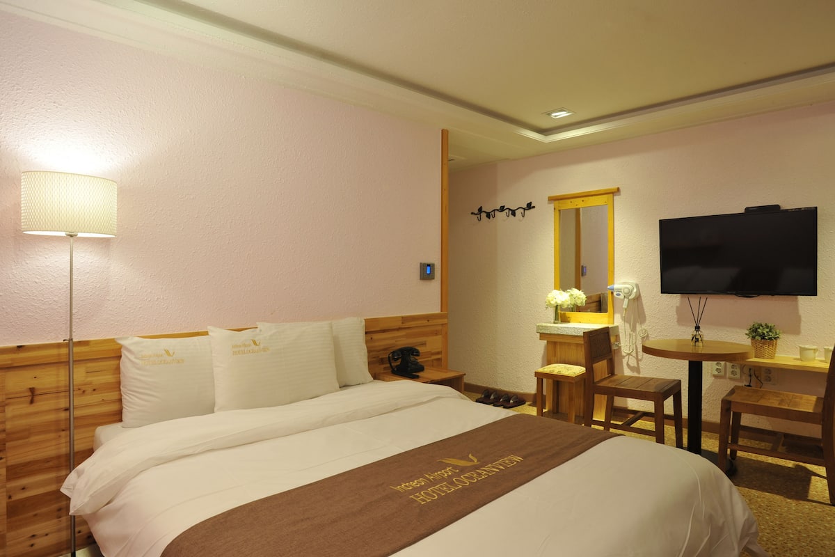 Una habitació d'hotel amb un llit, una taula de treball, una cadira, una televisió i una làmpada.