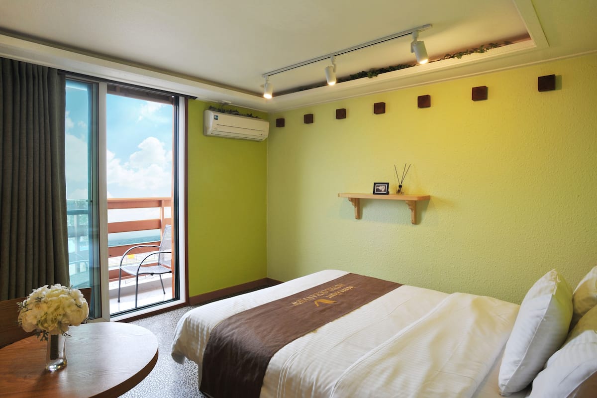 Habitació d'hotel amb un llit, una taula petita amb un ram, un balcó amb una cadira i una estant penjada a la paret amb un marc de foto.