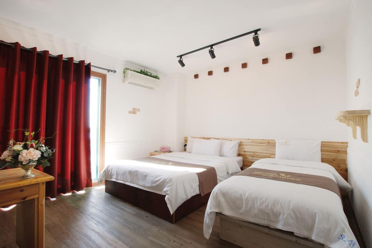 Una habitació d'hotel amb dos llits, un capçal de llit de fusta, una taula petita amb un ram de flors i una finestra amb cortines vermelles.