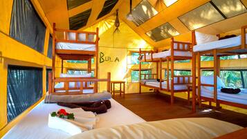 A dormitory-style room with bunk beds, a small table, and a wall with the word "BULA".