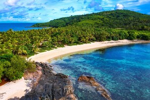 Una playa tropical con aguas turquesas cristalinas, una orilla arenosa y abundante vegetación.
