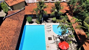 Vista aérea de una piscina con techos de azulejos, palmeras y sillas de descanso.