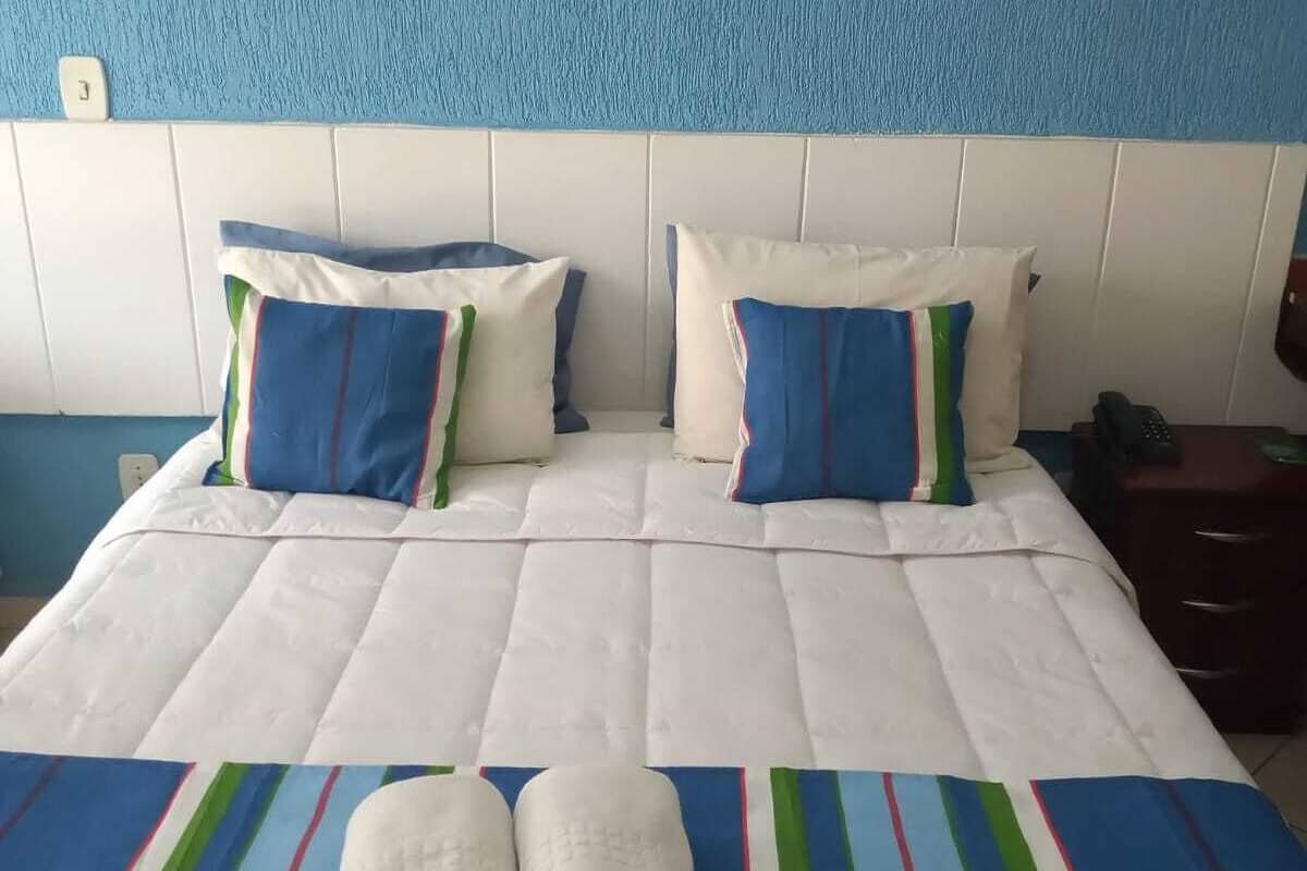 Ein ordentlich bezogenes Bett mit weißer Bettwäsche und blauen, grünen und roten Akzenten.