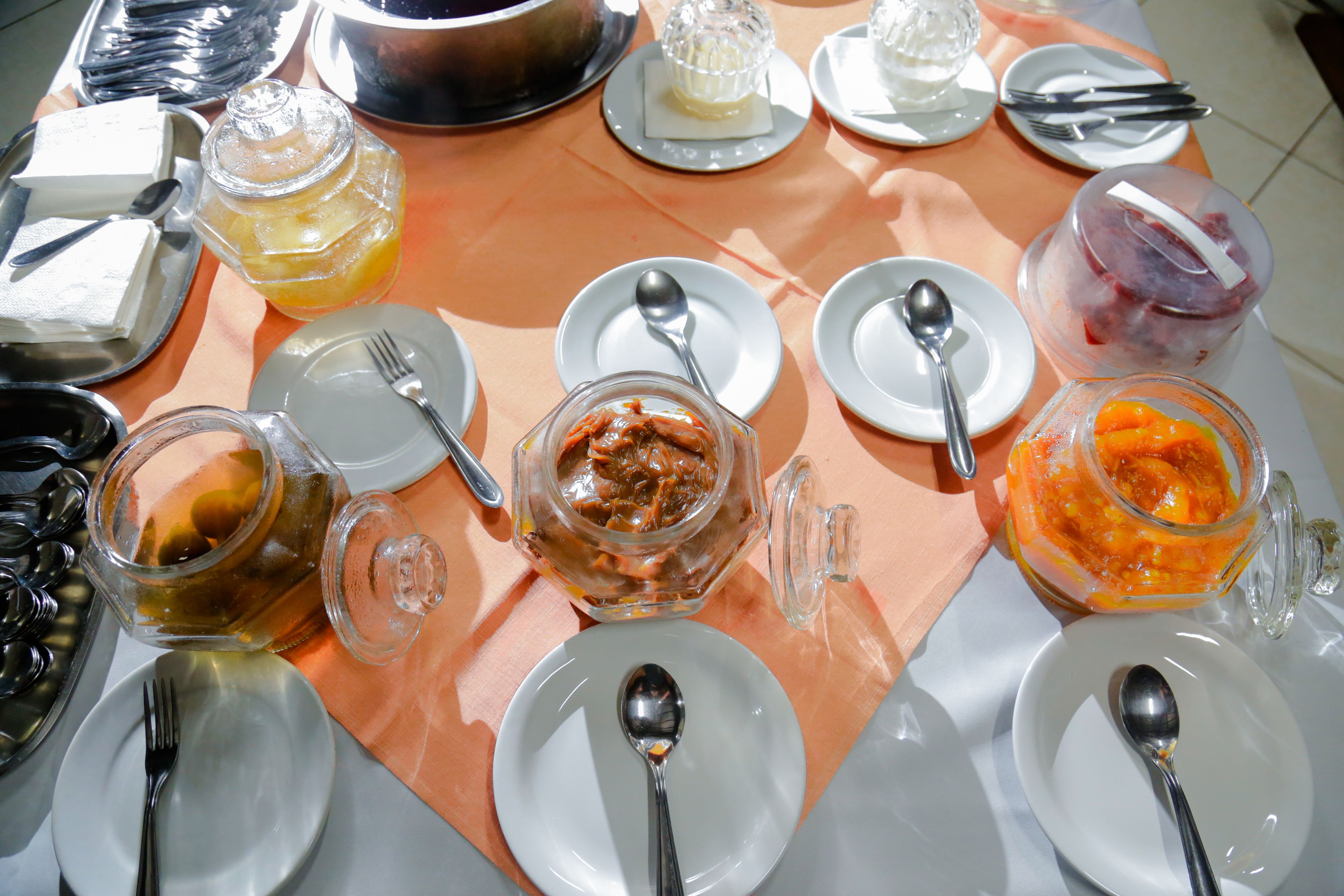 A table set with various food items and utensils, including plates, spoons, forks, and a glass jar with a lid.