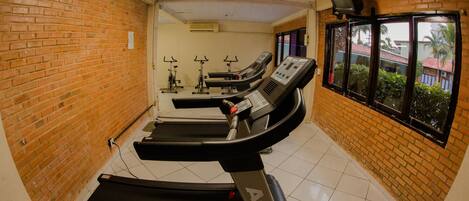 Un gimnasio con cintas de correr, bicicletas estáticas y un espejo grande.
