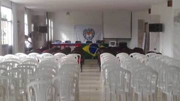 Un salón de conferencias con filas de sillas de plástico blancas, un atril con una bandera y una pantalla de proyector.