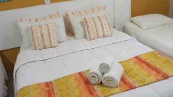 A hotel room with a large bed, two smaller beds, and a headboard with a yellow accent.