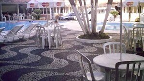 Un área junto a la piscina con sillones de descanso y mesas, suelo estampado y sombrillas con logotipos de Mastercard.