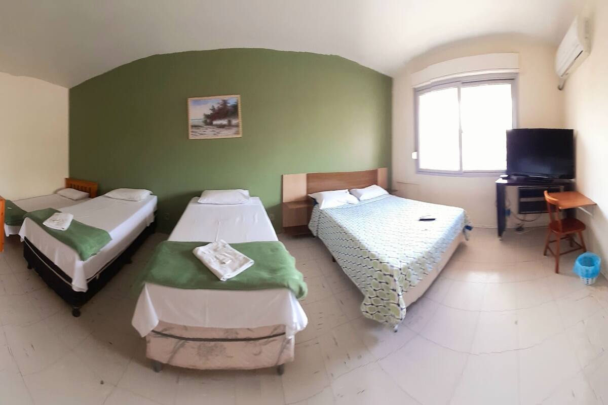 Quarto de hotel com duas camas de solteiro, uma televisão, uma escrivaninha e uma janela pequena.