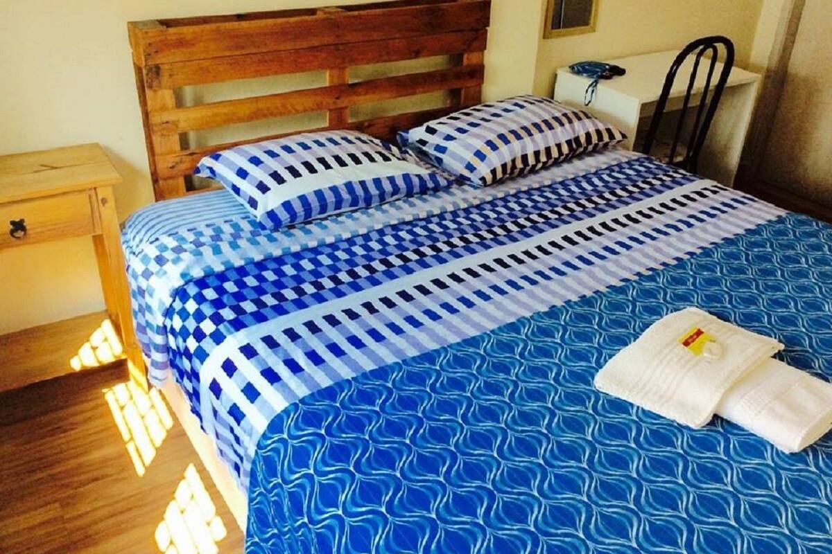 Uma cama com colcha xadrez azul e branca, cabeceira de madeira e duas almofadas.
