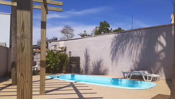 A backyard with a swimming pool, wooden pergola, and outdoor furniture. - Pousada Terra Sul (Porto Alegre)