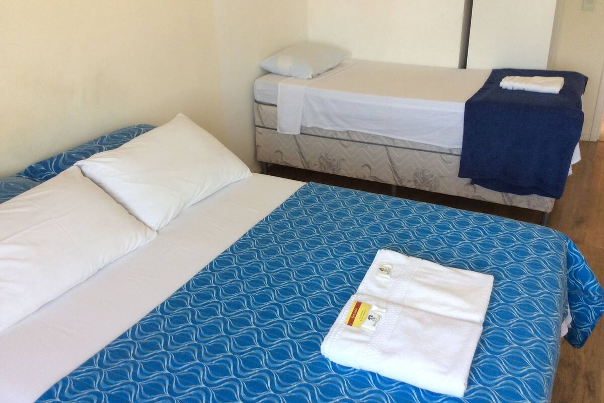 Quarto com duas camas, uma com colcha azul estampada e outra com colcha branca.