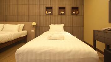 Habitació d'hotel amb un llit gran, un altre més petit, panells de fusta a la paret i una petita taula de nit amb una làmpada.