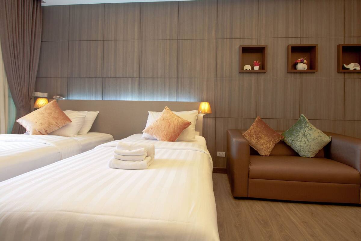 Habitación de hotel con dos camas, un sofá y estantes con adornos.
