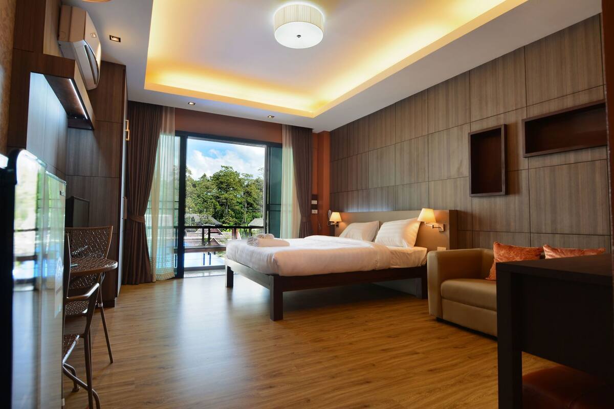 Habitación de hotel moderna con una cama grande, un sofá, un escritorio y un balcón con vistas a zonas verdes.