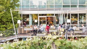 An outdoor dining area with tables and chairs, surrounded by greenery and a building with large windows. - Hotel Daniel Vienna (Vienna)
