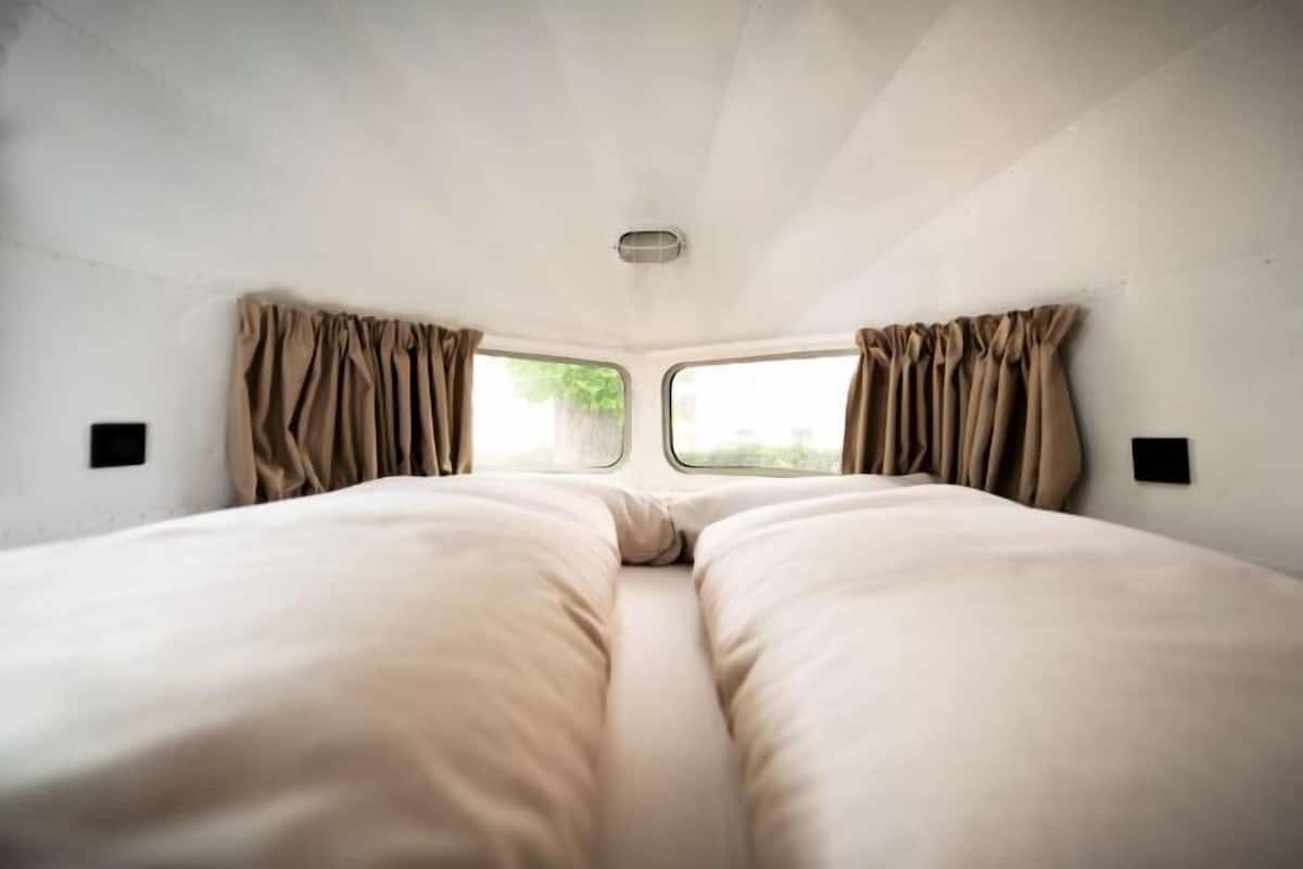 A bedroom with two beds, a window, curtains, and a ceiling light.